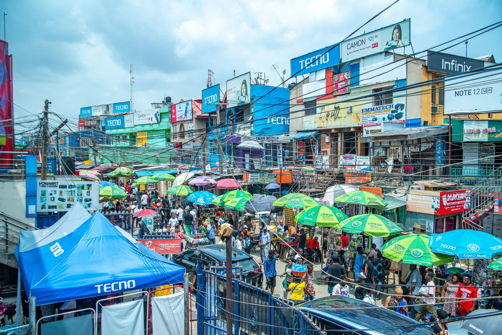 A busy Lagos market street seen from above, full of umbrellas and billboards.